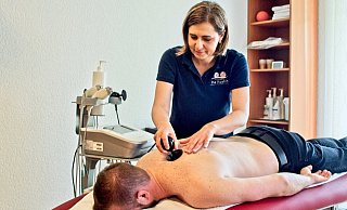 Ina Koshin (stehend) führt mit ihrem Kollegen Sergej Röhrig (liegend) die Anwendung der WINBACK Therapie vor. Der Körper wird über das Gerät bei der Behandlung stimuliert, der Patient fühlt eine leichte und entspannende Wärme. - Wencke Meckenstock