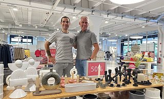 Timo Häberle, Leitung der Factory-Outlets bei Brax (links) und Geschäftsführer und Unternehmenssprecher Marc Freyberg im Herforder Outlet Im Kleinen Felde. Auf dem Verkaufstisch vor ihnen sind Artikel aus dem Bereich "Home & Living", also Dekorationsartikel für Zuhause, zu sehen. Auch dieses Sortiment ergänzt nun bereits das Kleidungsangebot. - Natalie Gottwald