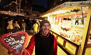 Marcus Notz aus Uslar bietet an seinem Stand Lebkuchenherzen und gebrannte Mandeln an, während im Hintergrund die Eröffnung des Höxteraner Weihnachtsmarkts läuft. - Davi Schellenberg