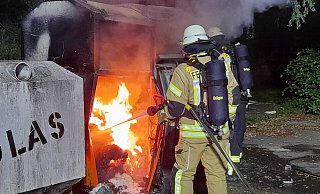 Flammen schlagen aus den beiden Altkleidercontainern, während Kräfte der Feuerwehr das Löschen starten. - Ralf Scholle