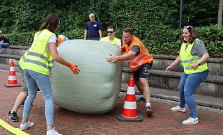 Mit vereinten Kräften rollen die Mitglieder der Gruppe „Pegelclub & Friends“ den rund 350 Kilogramm schweren Strohballen durch den Hindernis-Parcours auf dem Pemberville Platz. - Shannon-Lee Bendig