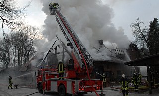 Riegelstellung: Da zwei Drehleitern vor Ort waren, die zweite ist wegen des Rauchs nicht zu sehen, konnte die Feuerwehr wirksam die umliegenden Gebäude auf dem Reiterhof Hachmann im Februar 2012 schützen, die durch Funkenflug stark gefährdet waren. - BIELEFELD