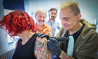 Milos tätowiert über Tattoos hinweg, damit diese nicht mehr zu erkennen sind - und hilft so bedürftigen Menschen, die unter Tattoos oder Narben leiden. Er ist Teil eines Projektes der Stiftung Solidarität von Vorstand Moritz Schön (2.v.r.). Sozialpfarrer Matthias Blomeier findet das Projekt wichtig, Nicole ist hier Fotomodell, sie liebt ihre Tattoos. - Sarah Jonek