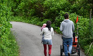Ein Paar mit Kind läuft eine schmale Straße entlang. Die aktuelle Elterngeld-Debatte trifft viele Familien. - picture alliance/dpa