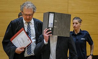 Der Angeklagte verdeckt sein Gesicht mit einem Ordner. Er soll seine Kollegin bei einer Party erstochen haben. - Andreas Zobe (Archiv)
