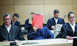 Prozess im Mai 2023: Einer der Angeklagten versteckt sein Gesicht hinter einem roten Aktendeckel. Er wird von den Strafverteidigern Detlev Binder (l.) und Susanne Renner vertreten. Hinter ihnen sitzt der zweite Angeklagte, der ebenfalls unerkannt bleiben will. Sie sollen einen Mann aus einem Flüchtlingsheim in Spenge entführt haben. - Sarah Jonek