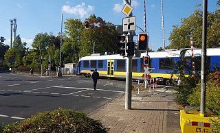 Der Zug überquert den Bahnübergang, obwohl die Schranken geöffnet sind. Ein Fußgänger beobachtet mitten auf der Fahrbahn stehend diese Situation. - Wolfgang Döbber