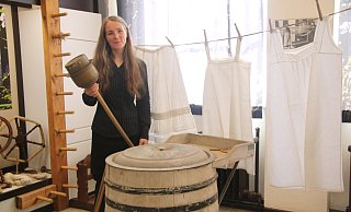Museumsleiterin Sonja Voss in dem Bereich der Ausstellung, der sich mit dem Thema Waschen beschäftigt. In der Hand hält sie eine Waschglocke, vor ihr steht eine alte Waschmaschine. - Anthea Moschner