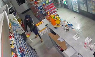 Auf dem Überwachungsvideo ist zu sehen, wie ein vermummter Mann eine Flüssigkeit - vermutlich Brandbeschleuniger - verspritzt. - Polizei/Screenshot