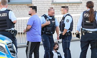 Polizisten am Tatort. Ein festgenommener Mann sitzt auf dem Boden. - Claus Frickemeier