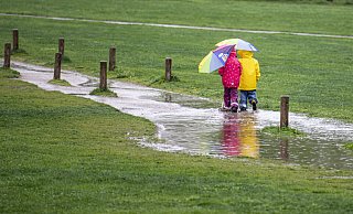 Zwei Kinder laufen in einem Park durch eine große Pfütze. - Fabian Sommer