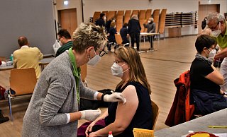 Hildegard Stallein gibt die Corona-Impfung in den Arm einer Patientin. Im Hintergrund warten bereits die nächsten Impfwilligen an der Anmeldung. - Raphael Athens