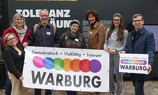 Judith Schlinker (Cineplex; v. l.), Anke Schekahn (Buntes Warburg), Wilm Pollmann (Warburger Hanse), Kathrin Helg (Buntes Warburg), Corinna Wieczorek (Sekundarschule), Selina Knipping (Warburger Hanse) und Bürgermeister Tobias Scherf mit dem neuen Logo. - Buntes Warburg