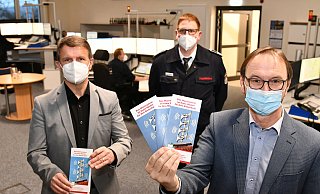 Landrat Michael Stickeln (l.) und Matthias Kämpfer (r.) zeigen den neuen Flyer. Mit seinem Team koordiniert Leitstellenleiter Jürgen Romund die Auslösung der über 160 Sirenen im Kreis. - Kreis Höxter