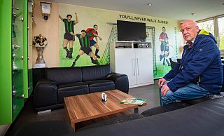 Vor dem Torszenen-Gewinnerbild: Dornbergs Vorstandsmitglied Thomas Nottebrock macht es sich auf dem Sofa bequem. An der Wand hängen mit Pokalen gefüllte Vitrinen. Foto: Mike-Dennis müller - Mike-Dennis Müller / www.mdm.photo