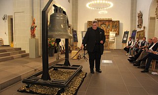 Monsignore Georg Austen, Generalsekretär des Bonifatiuswerkes, läutet die #PeaceBell zur Eröffnung der Ausstellung in der Gaukirche am Freitagabend. Am kommenden Mittwoch ist der Künstler Michael Patrick Kelly bei einem internationalen Friedensgebet im Paderborner Dom selbst zu Gast. Foto: Bonifatiuswerk/Matthias Band - Bonifatiuswerk/Matthias Band
