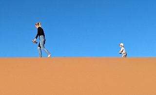 Angekommen im größten Sandkasten der Welt, der Sahara: Mutter und Kind spazieren vor leuchtend blauem Himmel durch die Dünen. - privat