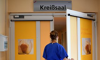 Eine Klinik-Mitarbeiterin steht vor dem Kreißsaal. Die Aufklärungsbögen für eine mögliche Schmerzhemmung durch Periduralanästhesie (PDA) werden links in den Postkasten eingeworfen. - Britta Pedersen/dpa