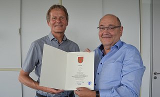 Ludwig Koch (l.) nimmt vom Dezernenten Wolfgang Walter die offizielle Urkunde zum Ruhestand entgegen. - Stadt Paderborn