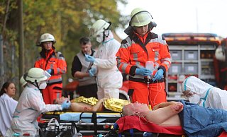 Rettungskräfte sind mit weißen Schutzanzügen bekleidet, um die Verletzten aus möglicherweise kontaminiertem Qualm zu holen. Reibungslos läuft das Zusammenspiel zwischen Rettungsdienst und Einsatzkräften der Feuerwehr. - Charlotte Mahncke