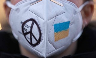 Eine Frau trägt während einer Demonstration eine FFP2-Maske, auf die das Peace-Zeichen und die ukrainische Fahne gemalt sind. Tatsächlich hat der Krieg in Osteuropa Auswirkungen auf die Corona-Situation in Deutschland. - AFP or licensors