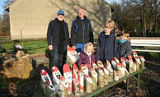 Viele kleine Weihnachtsmänner - auf unserem Foto sind nicht alle zu sehen - schmücken den Dorfplatz in Herringhausen. Karl-Heinz Pöninghaus (hinten links) und Frank Beckhoff haben den vielen Kindern, hier vertreten durch Line, Lias und Janis, geholfen. - Karin Wessler