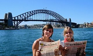 Simone Trysna (l.) und Laura Delkeskamp haben im Weihnachtspaket der Eltern die Neue Westfälische gefunden – und informieren sich vor der Harbour Bridge in Sydney über die Kurstadt. - FOTO: PRIVAT