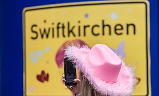 Ein Fan fotografiert vor dem Konzert der Sängerin Taylor Swift in Gelsenkirchen ein «Swiftkirchen»-Schild. Während des Konzerts am Abend zog der Datenverbrauch in den Handynetzen in der Veltins Arena kräftig an. - Oliver Berg/dpa