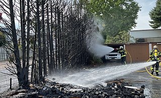 Einsatzkräfte der Freiwilligen Feuerwehr Leopoldshöhe und Oerlinghausen löschen den Heckenbrand unweit des Postverteilzentrums in Asemissen. - Freiwillige Feuerwehr Leopoldshöhe