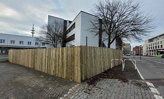 Ein zwei Meter hoher Bretterzaun kündigt den Start der Arbeiten auf dem Postareal an. - Ludger Osterkamp
