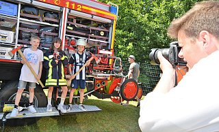 Eingefangen: Felix Hano (r.) fotografiert Ben Brink (11), Emma Klausing (11) und Silas Steinbeck (12, v. l.) vor einem Feuerwehrauto mit Gerätschaften, Jacke und Helm. Beim Feuerwehrfest dürfen die Kinder in die Rollen der Kameraden schlüpfen. - Karin Prignitz