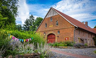 Der Namensstein auf der Pflanzeninsel vor dem Haupthaus von Hof Ramsbrock ist von Wildblumen fast überwucher, das springende Schaf kaum noch erkennbar. - Mike-Dennis Mueller / www.mdm.photo