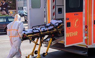 Infektionstransport: Ein Notfallsanitäter in Schutzkleidung schiebt die Trage zurück in den Rettungswagen, in dem zuvor eine infizierte Person transportiert wurde. - Christian Mathiesen