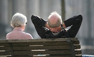 Ein Rentnerpaar sitzt auf einer Bank und sonnt sich. - dpa
