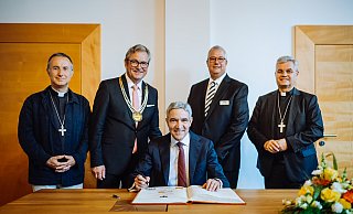 Vor seiner Festrede trägt sich Stephan Harbarth, Präsident des Bundesverfassungsgerichts, ins Goldene Buch der Stadt Paderborn ein. Hinter ihm stehen Jean-Pierre Vuillemin Bischof von Le Mans (v. l.), Bürgermeister Michael Dreier, Gildemeister Johannes Beverungen und Erzbischof Udo Markus Bentz. - Besim Mazhiqi