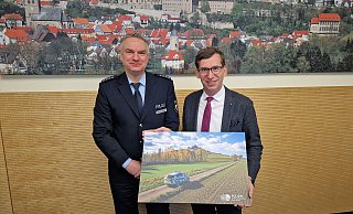 Ein Geschenk für das Stadthaus als Zeichen für die gute Zusammenarbeit: Georg Arendes, Leiter der Polizeiwache Warburg, übergab Bürgermeister Tobias Scherf ein Bild, das ein Fahrzeug der Polizei vor dem Desenberg zeigt. - Stadt Warburg