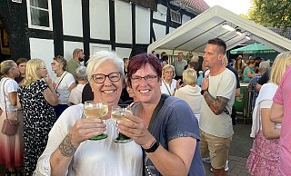Die Schwestern Nicole Krüger (l.) und Martina Buchholz sind Stammgäste auf dem Rehmer Markt. Sie stoßen mit einem Weißwein darauf an, auch dieses Jahr wieder viele Bekannte rund ums Heimathaus zu treffen. - Nicole Sielermann