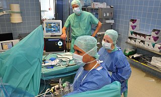 Oberarzt Fadi Nazha (vorne) sieht auf dem Bildschirm, wie er das Instrument durch die Harnröhre schiebt. Operationstechnische Assistentin Vanessa Wünsche reicht Instrumente an. Chefarzt Andreas Kutta steht neben dem Lasergerät. - Brüderkrankenhaus St. Josef