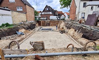 Die teilweise mit weißem Sand verdeckten dunklen Bögen links und rechts der Baugrube dokumentieren das Profil des doppelten Stadtgrabens. - Birgit Vredenburg
