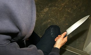 Ein Mann mit Kapuze hält ein Messer in der Hand. - picture alliance / empics