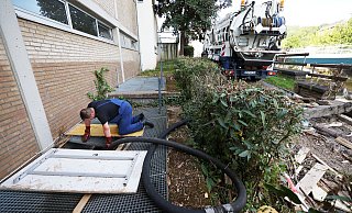 Ein Mitarbeiter des Spezialentsorgers hält an einer Schule den Schlauch in den Keller. - picture alliance/dpa