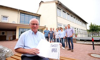 Hans-Josef Held (vorn) zeigt die entscheidende Seite in der Godelheimer Chronik, in der über die Eröffnung der Schule berichtet wird. Zum runden Geburtstag planen er und seine Mitstreiter ein buntes Fest. - David Schellenberg
