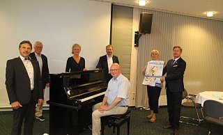 Jürgen Vieker (Sparkassenstiftung), Georg Droste (Rotary Club), Bärbel Kloss (Sparkassenstiftung), Ulrich Beckschewe (Rotary Club) und Heinz-Hermann Grube (am Klavier) sowie Antje Rohlfing (Hospiz Veritas) laden zum diesjährigen Solista-Konzert am Sonntag, 20. September, in der Stadthalle Lübbecke ein. - Klaus Frensing