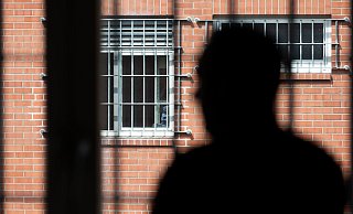 Ein Insasse steht vor einem vergitterten Fenster in der Unterbringungseinrichtung für Ausreisepflichtige in Büren. - Friso Gentsch/dpa