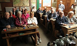 Die Gruppe der früheren Schülerinnen und Schüler nahm brav in der Klasse Platz. Anton Hillebrand (stehend) vom Bernhard-Wolff-Schulmuseum sorgte dafür, dass viele Erinnerungen aufgefrischt wurden. - Johannes Büttner