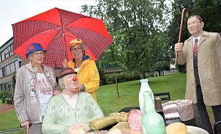 Marlis Brink (l.) und Sylvia Westhoff haben sich symbolisch bunte Karnevalshüte aufgesetzt und den Regenschirm aufgespannt. Vor ihnen sitzt am Tisch der Alltagsmenschen, mit roter Nase, die Stukenbrocker Närrin. - Karin Prignitz
