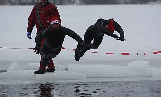 Die DLRG-Schwimmer Rainer Fleer (l.) und Michael Dressler hechten in das von den dicken, im Hintergrund liegenden Eisschollen befreite Loch. Die Mützen bleiben übrigens trotz des Sprunges auf den Köpfen. - FOTO: SVEN TIEKÖTTER
