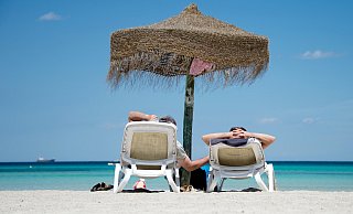 Zwei Urlauber genießen die Sonne am Strand – Last-Minute-Angebote machen spontane Erholung möglich. - Julian Stratenschulte/dpa/dpa-tm