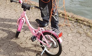 Ein Polizist steht am Mittellandkanal in Minden neben einem Kinderrad. Es war einer Vierjährigen ins Wasser gefallen. Foto: Polizei Duisburg/dpa - Polizei Duisburg
