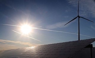 Ein Windrad steht hinter den Solarzellen einer Solarkraftanlage im Sonnenschein. - Foto: Karl-Josef Hildenbrand/dpa